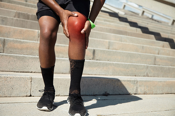 Homem atleta com a mão no joelho esquerdo que está vermelho e machucado