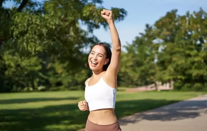 mulher-asiatica-de-top-branco-e-fones-de-ouvido-comemorando-durante-sua-corrida-em-um-parque